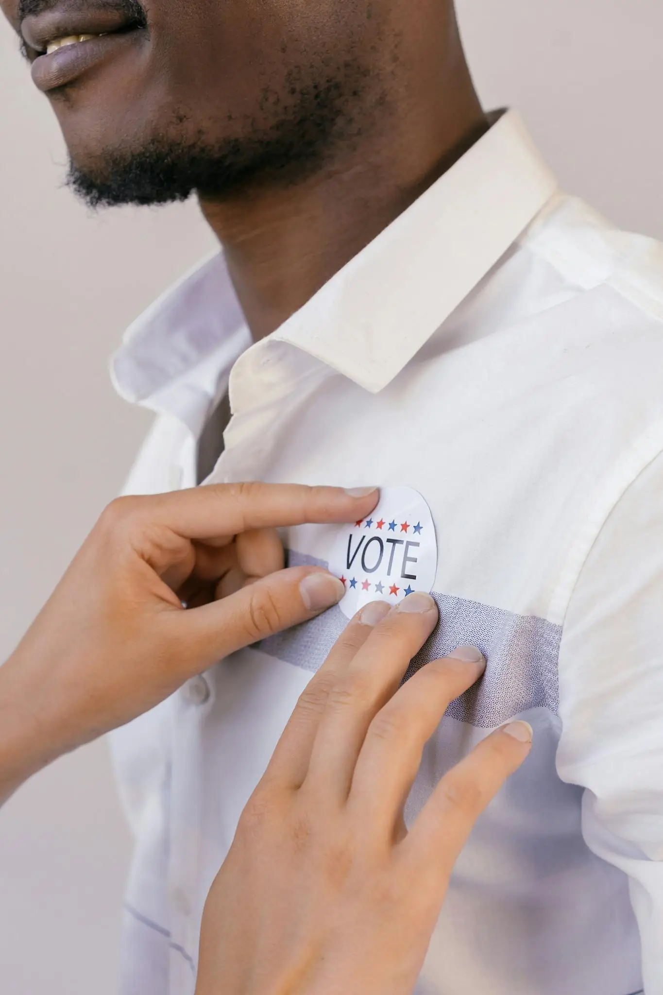 Hands placing a vote button on a shirt symbolizing participation in democracy.